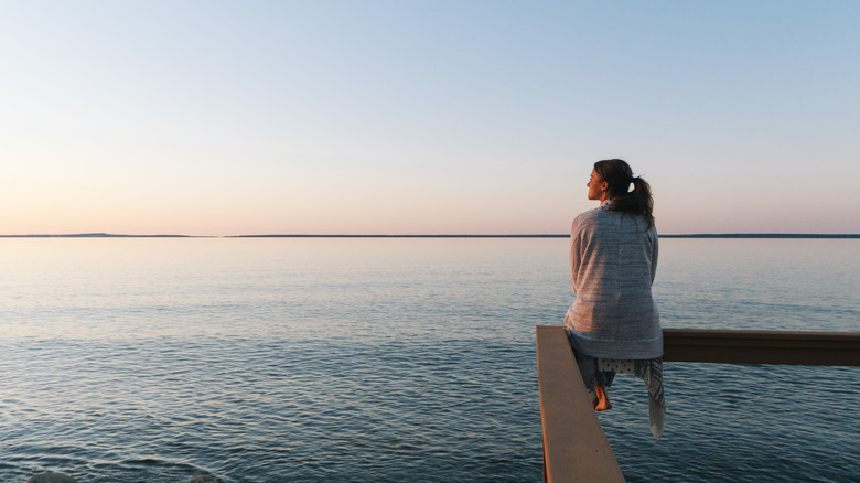 A woman sitting on the railing of an observation deck overlooking one of the Great Lakes