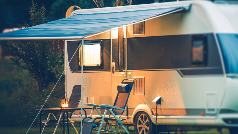 A parked RV with an awning out over two chairs and a small table