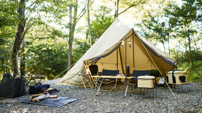 Tan colored tent set up in the woods with folding table and chairs.