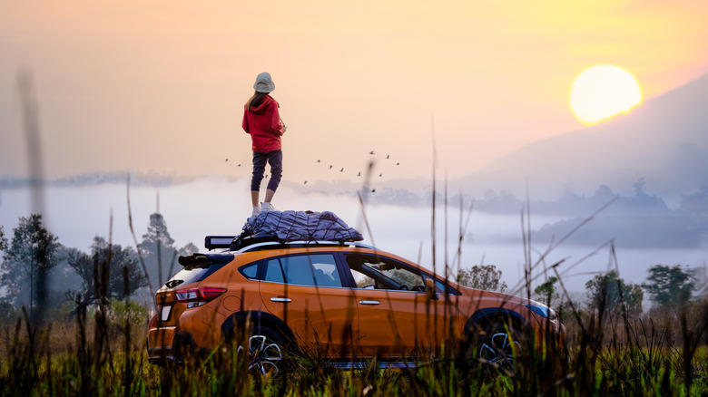 woman stands on her car in the wilderness