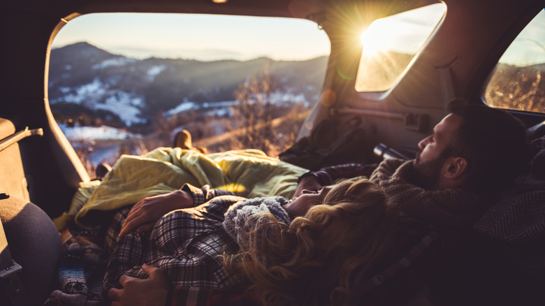 man and woman sleep in their car at a campsite