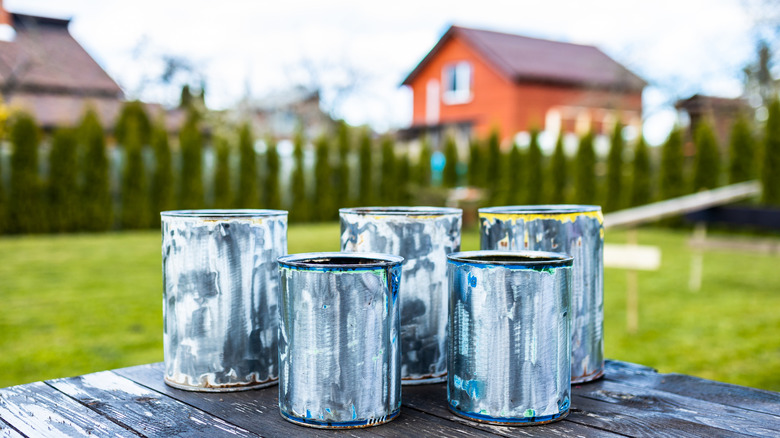Used paint cans on a table out in the back yard with hedges and other homes in the background