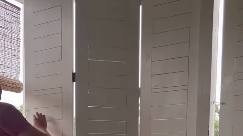 Person extending DIY privacy screen shutters on a porch