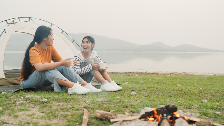 A campsite with two of people smiling and talking around a fire.