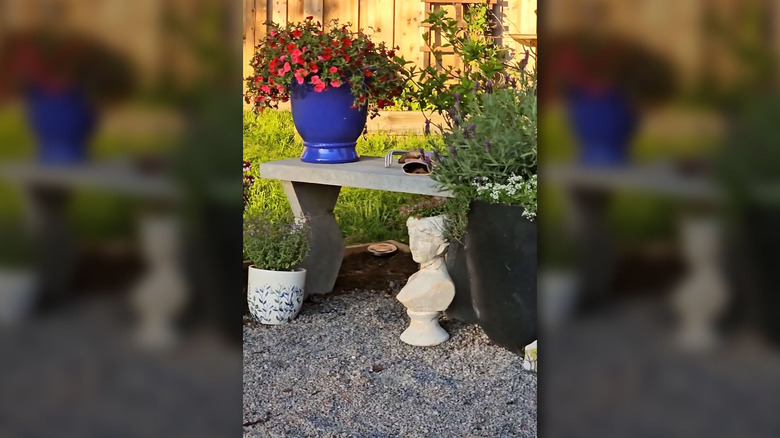 A DIY concrete bench holding potted flowers and garden tools.