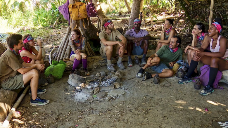 Survivor tribe members sit around fire 