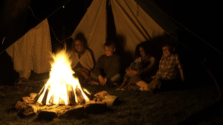 Four kids enjoying a campfire at night in front of tent