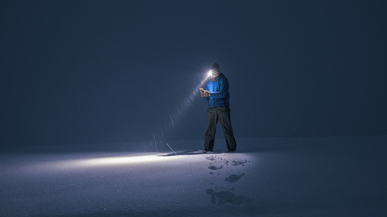 Person looking at a device with their headlamp on in a snowstorm