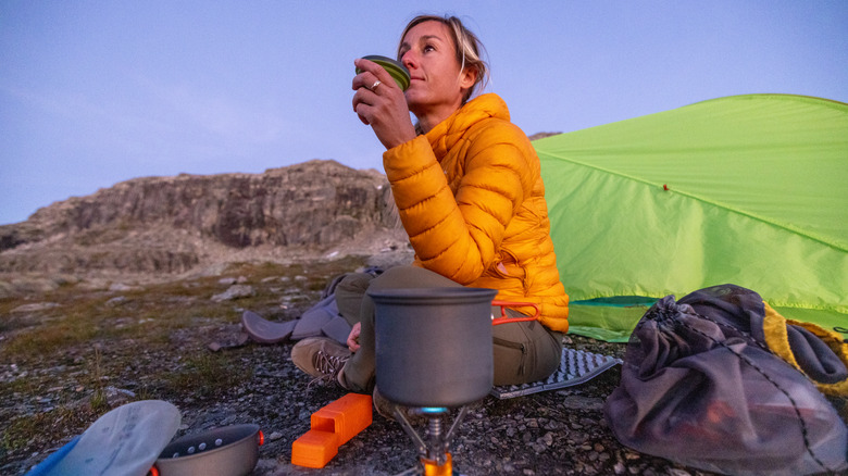 Backpacker drinking from a cup in front of their tent