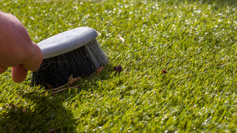 Person using a scrub brush to clean artificial turf