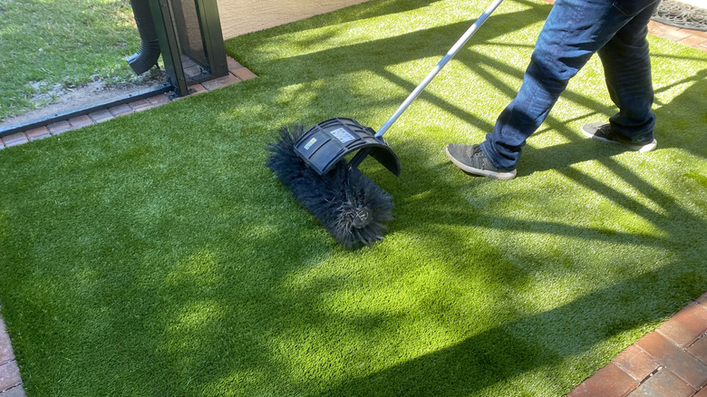 Person using an artificial turf push brush to maintain the turf