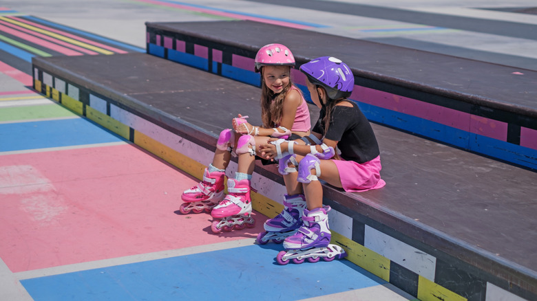 A pair of children clad in roller skates and protective gear, at a local skate park