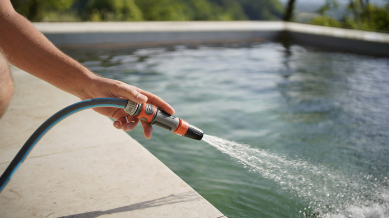 Person filling pool with a dark-color garden hose
