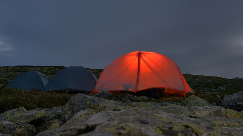 A group of tents placed along a mountain ridge. One is glowing with interior light