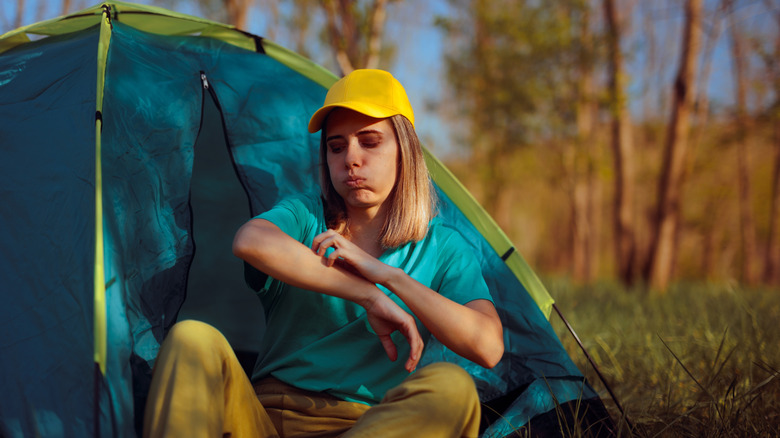 Woman scratches bug bite outside tent