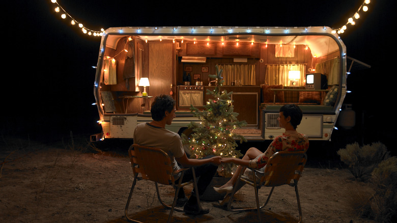 A couple sit outside a lighted camper, during a dark evening
