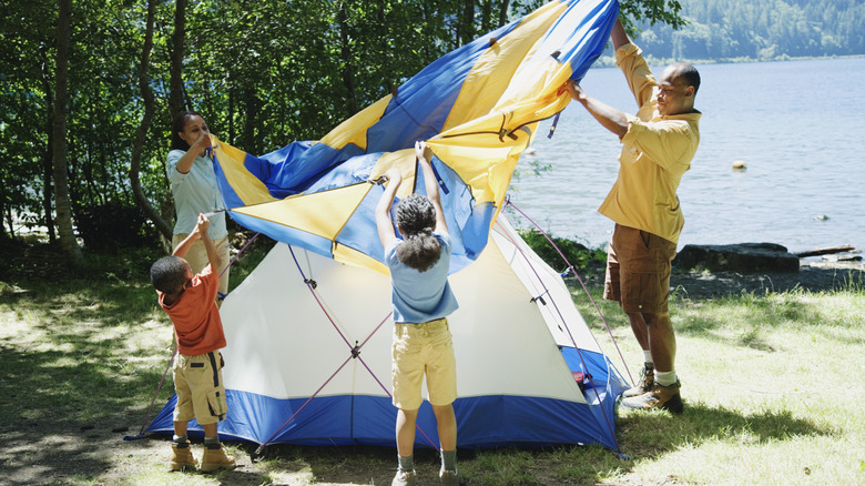 A family works together to put the finishing touches on a tent, near a body of water