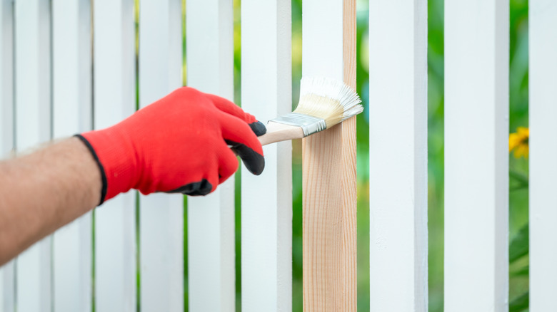 A person paints the planks of a wooden fence