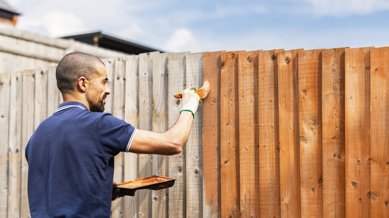 A man paints one side of a fence outside