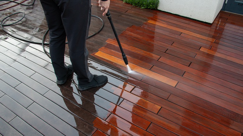 A homeowner pressure washing a wooden deck