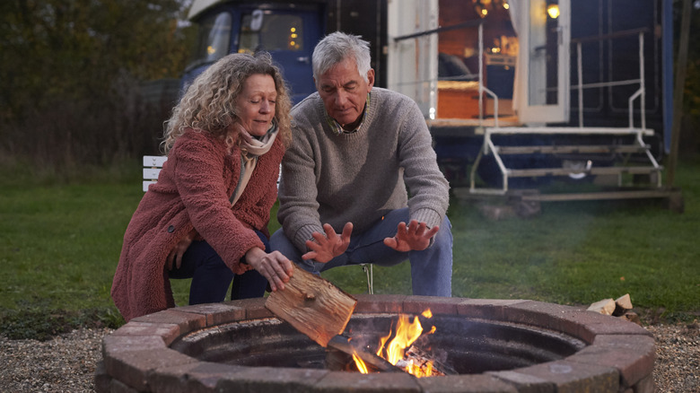 Couple placing a log on a fire pit
