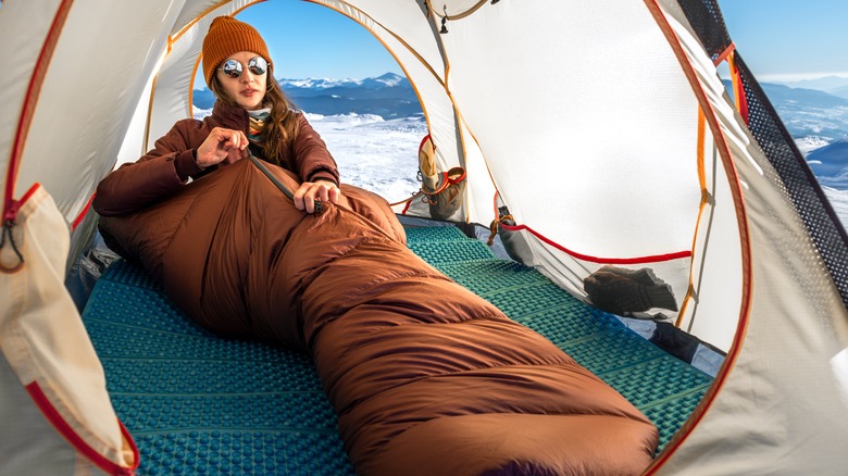 Woman zips sleeping bag at sunset