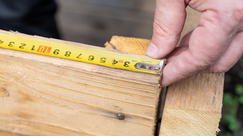 Close-up of a hand using a measuring tape to measure wooden boards