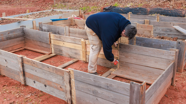 A man bending over and building a wooden frame for a raised garden bed