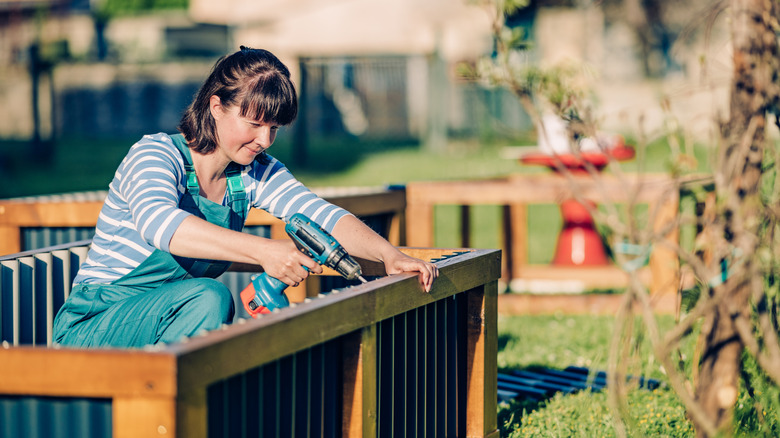 A woman building a raised garden bed with a drill on a bright day
