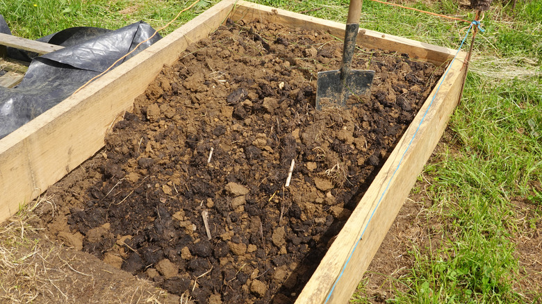 A wooden raised garden bed in the process of being filled with soil by a shovel