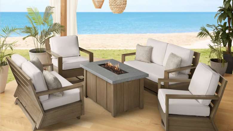 The Valmar 5-piece outdoor patio fire seating set from Agio, on a wooden deck with a beach in the background