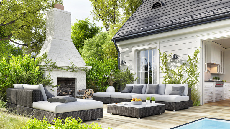 An outdoor patio with luxury furniture and a large fireplace with white-brick chimney