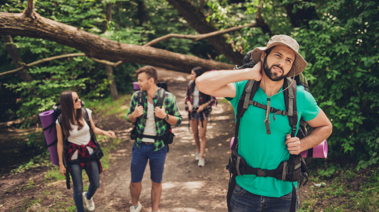 Man hiking with a group, slapping a mosquito on his neck