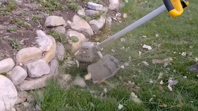 DeWalt string trimmer cutting grass around a rock wall