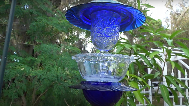A photo of a birdfeeder hanging outside that has been made with blue and clear glassware.