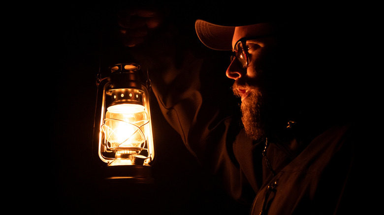 Man holding an oil lamp in darkness outside