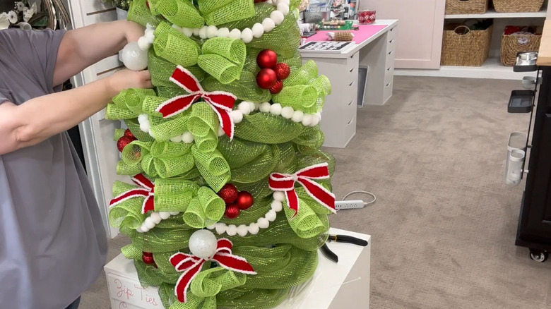 Someone decorating a DIY Christmas tree made from a tomato cage