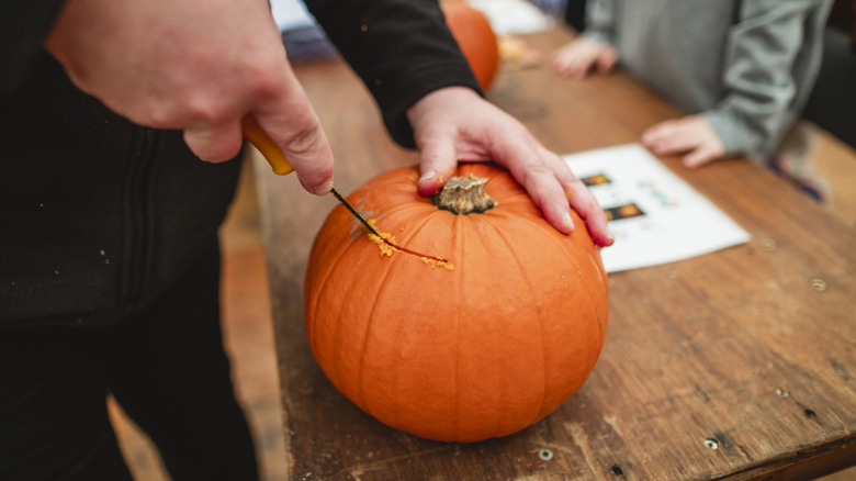 Someone carving out the top of a pumpkin
