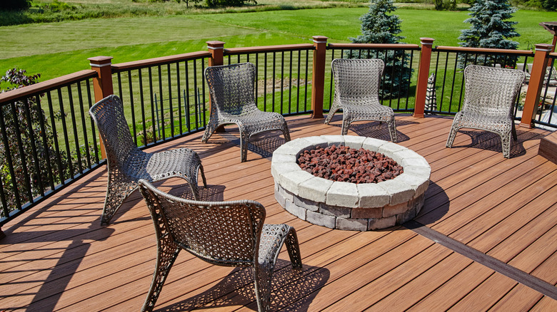 A fire pit filled with lava rocks surrounded by chairs on a porch