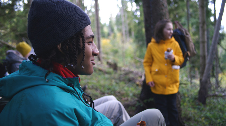 campers with green and yellow rain jackets sitting and smiling in wooded area.
