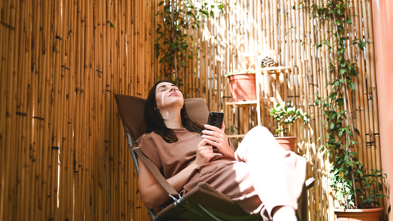 A woman enjoys her outdoor space with a seating area and climbing vine plants