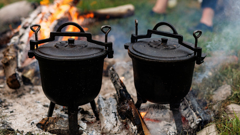 Two cast iron pots cooking on campfire