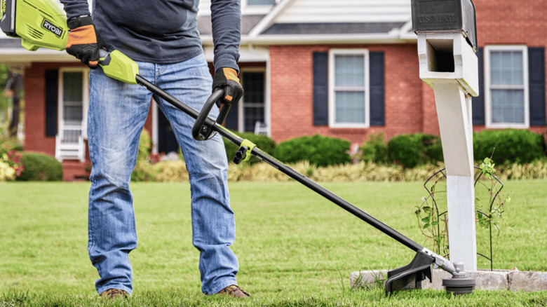 Person using Ryobi electric grass trimmer around a mailbox