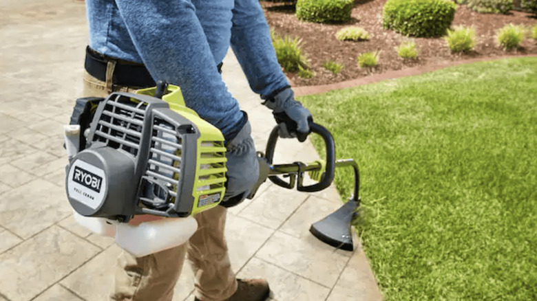 Person using a Ryobi 2-cycle gas trimmer on a lawn