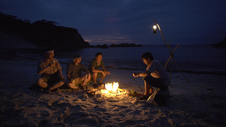 Four men sitting around a campfire on a beach
