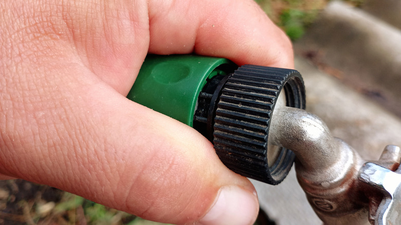 A hand gripping an outdoor faucet connector