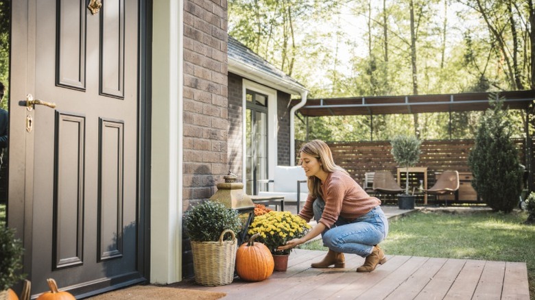 A woman arranging fall decor on front porch