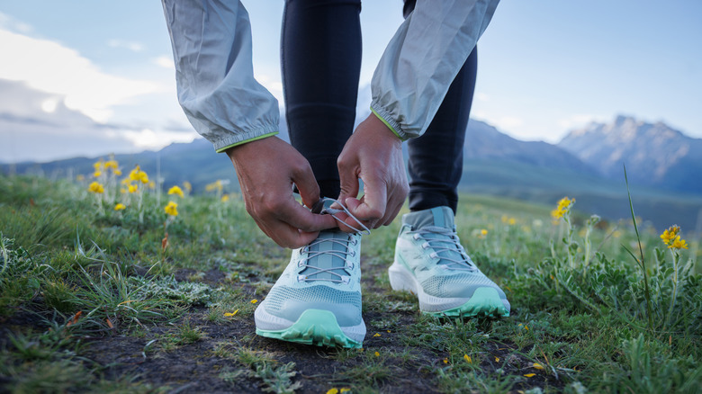 A runner stops to tie their trail runner sneakers