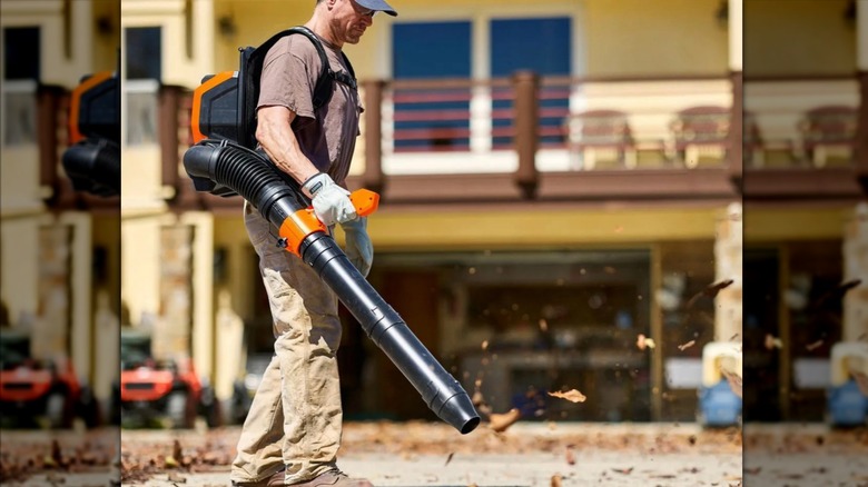 Man using the Atlas 80V dual-port backpack blower kit leaf blower on a leaf-covered driveway