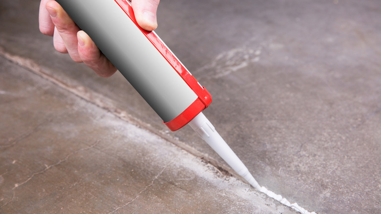 Person sealing a crack in concrete with a caulking gun